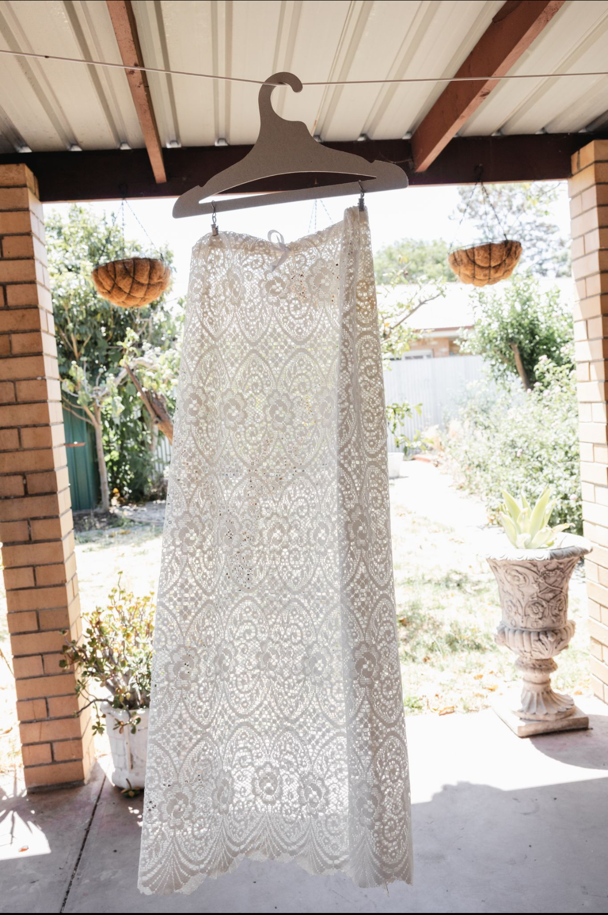 White lace wedding dress hanging on a hanger outdoors.