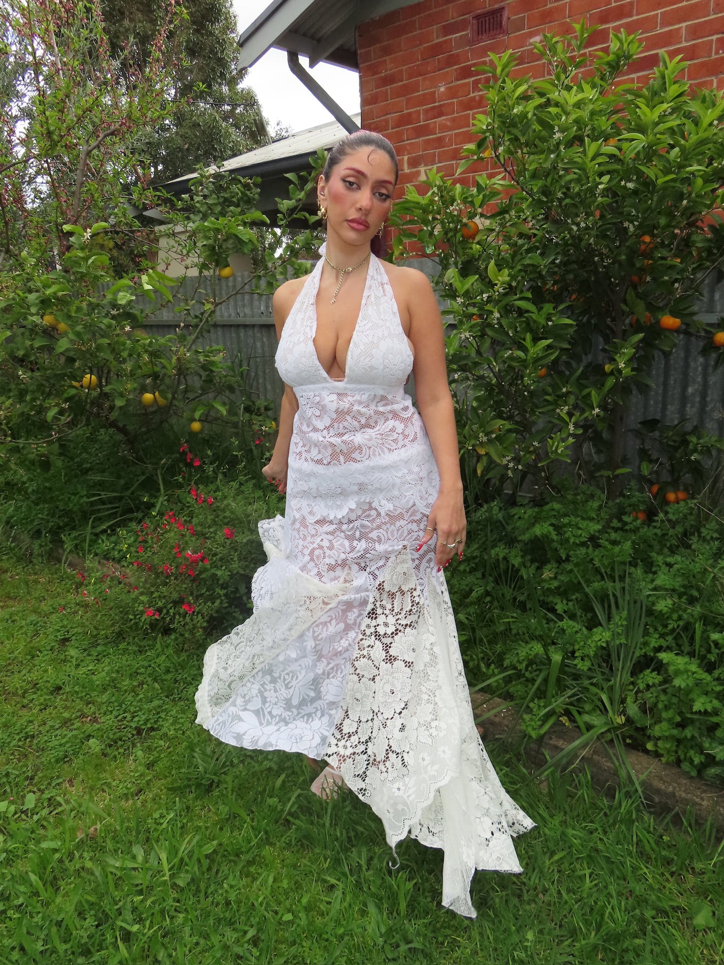 Woman in a white lace dress standing outdoors in a garden.