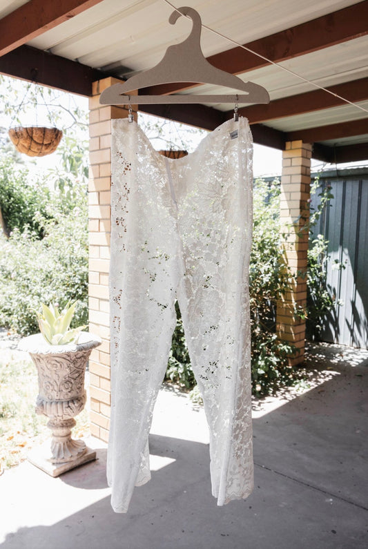 White lace garment hanging on a wooden hanger against a brick wall and outdoor setting.