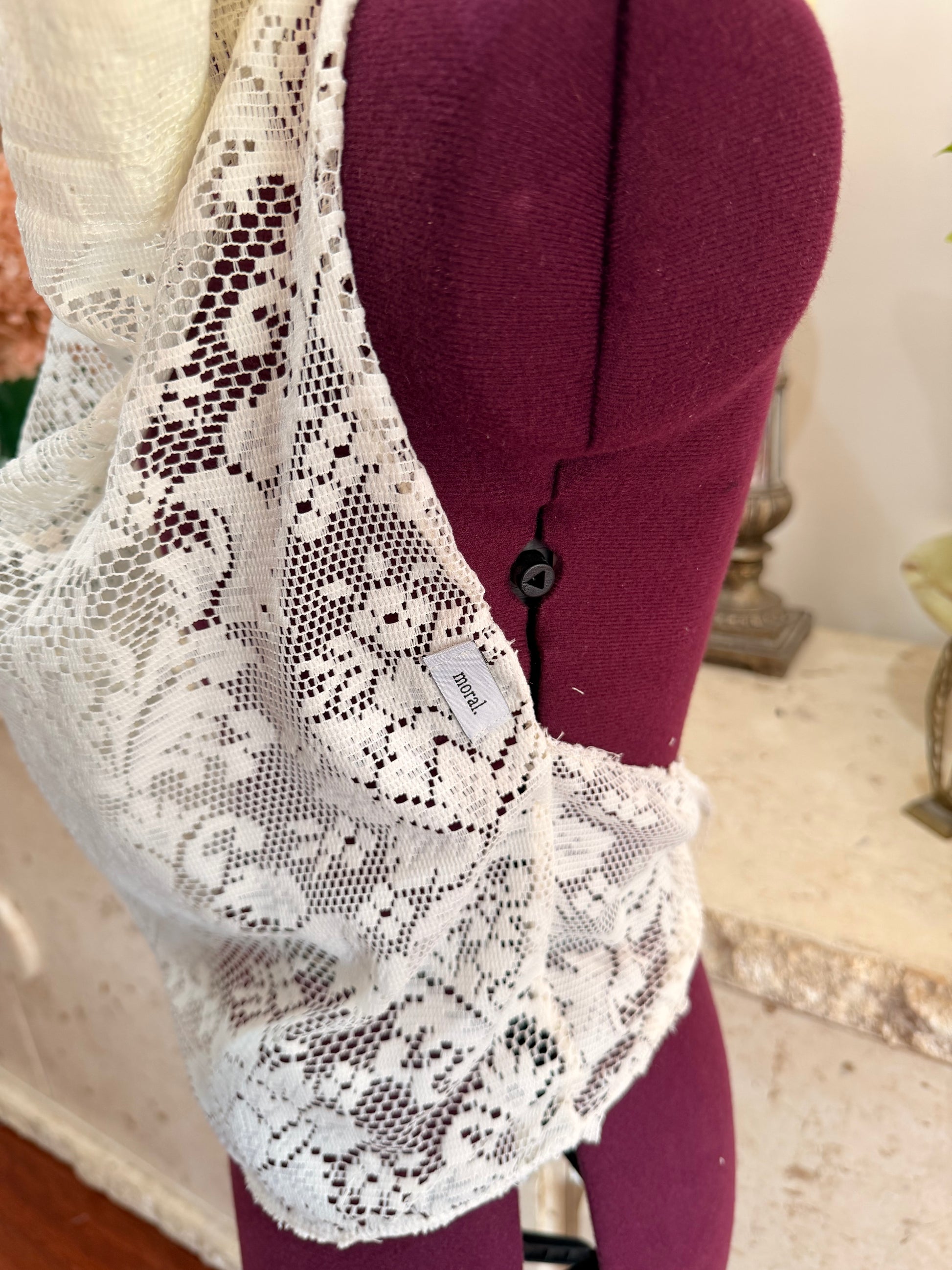 White floral lace trim draped over a burgundy fabric-covered dress form, with a small sewn label visible.